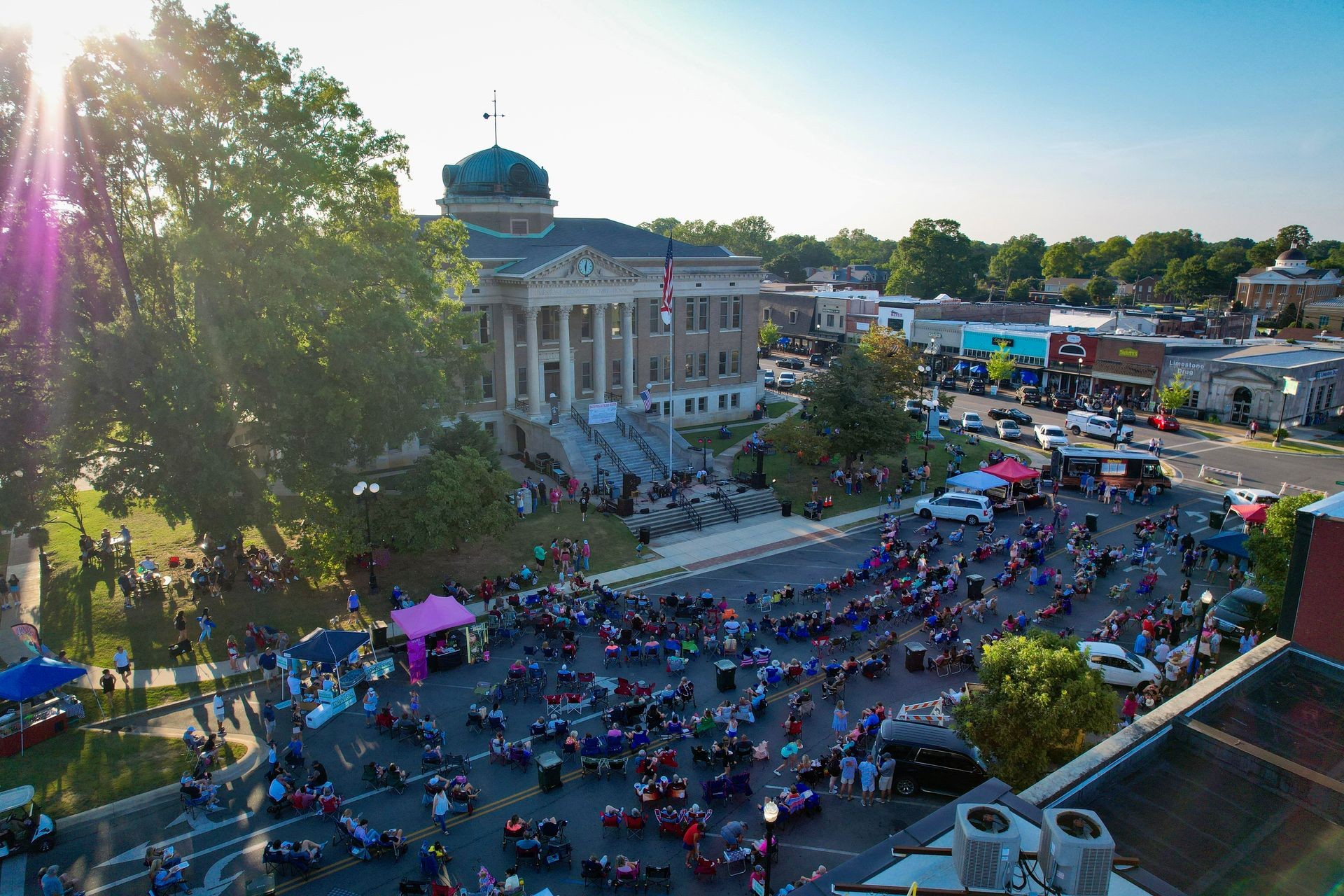 Aerial view of a town square event with people gathered around a courthouse on a sunny day.